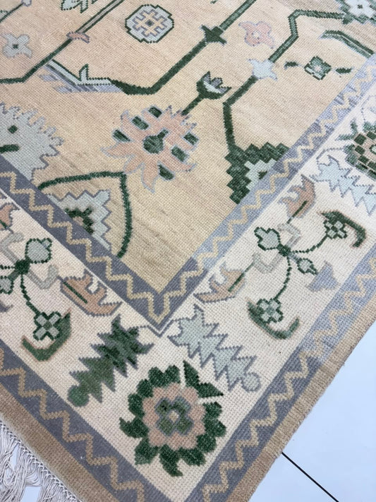 Beige Oushak-inspired rug corner with sage green motifs and fringed edge