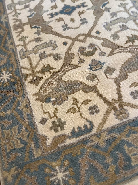 Handmade tribal rug with animal motifs and dusty blue border on ivory background