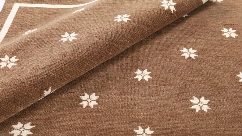 Folded edge of a brown and ivory floral rug showing its texture.