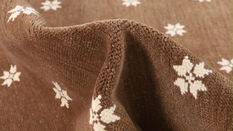 Detailed view of an ivory flower motif on the brown rug surface.