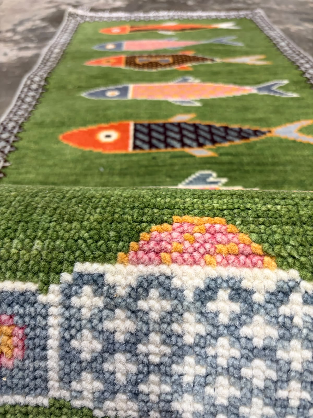 Close-up of colourful fish motifs on a green hand-knotted wool runner rug
