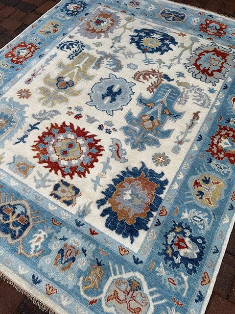 Angled view of handmade ivory blue Oushak rug with traditional floral motifs and artisan woven texture