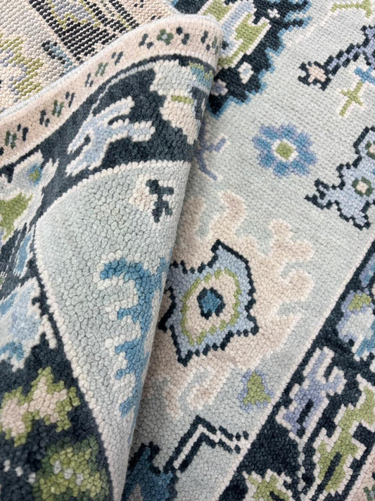 Handmade Scandinavian folk art wool rug with ice blue background, charcoal floral border and sage green accents.