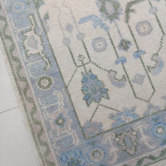 Close-up corner detail of ivory and blue Oushak rug with sage green border