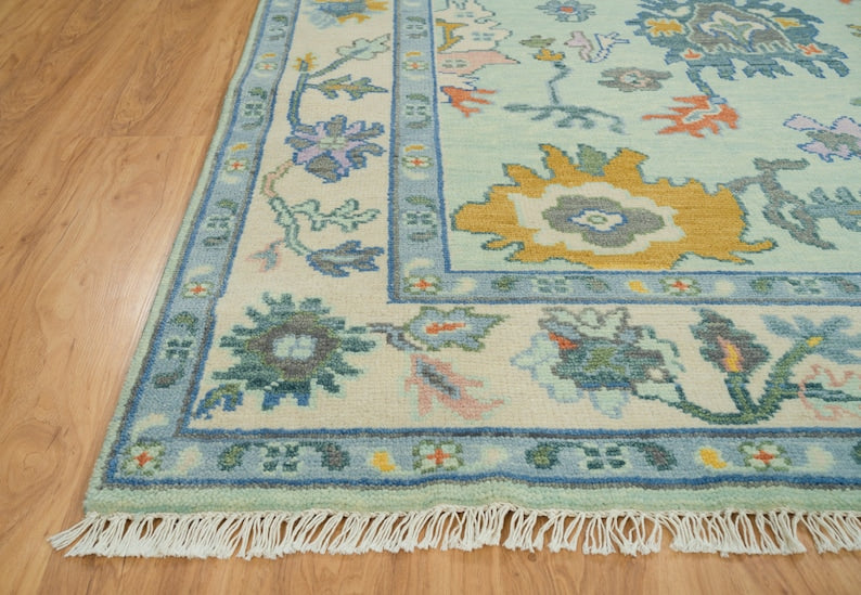 Close-up of the ivory floral border, blue edging and cream fringe on a mint green Oushak rug