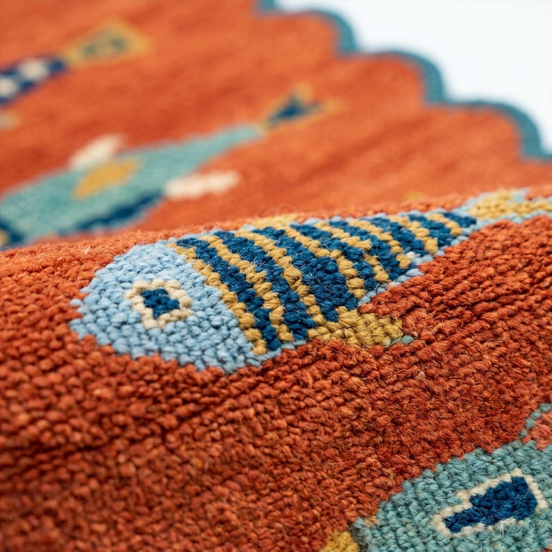 Close-up of a textured woven rug featuring stylized fish motifs in blue, yellow, and teal on a rust-orange background.