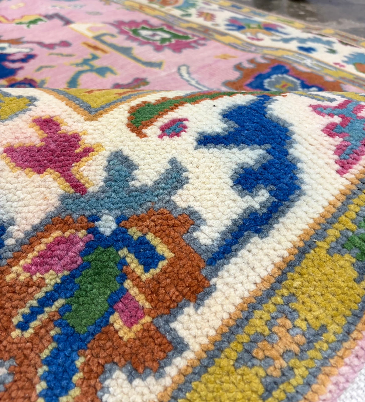 Close-up of colourful floral motifs and decorative patterns on a pink Oushak rug