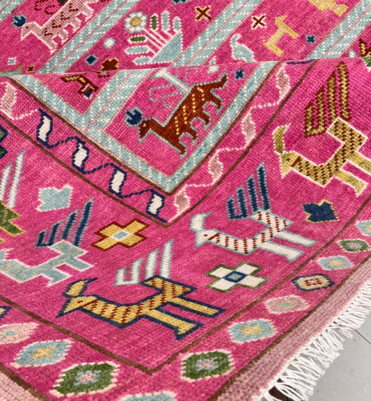 Angled view of pink tribal Oushak rug showing overall pattern and borders