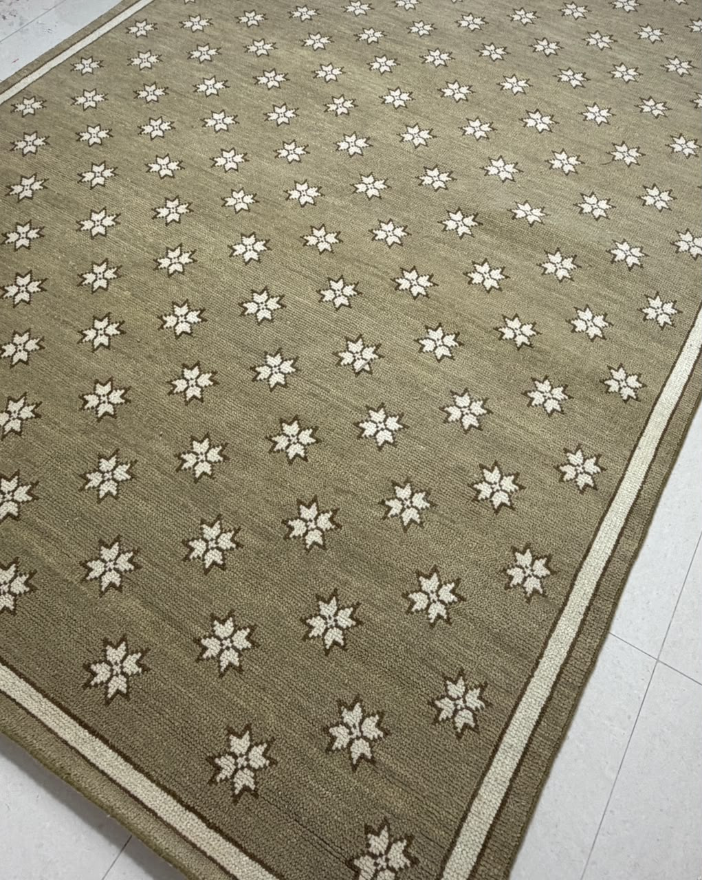 Angled view of taupe geometric area rug with ivory stars and a narrow contrasting border.