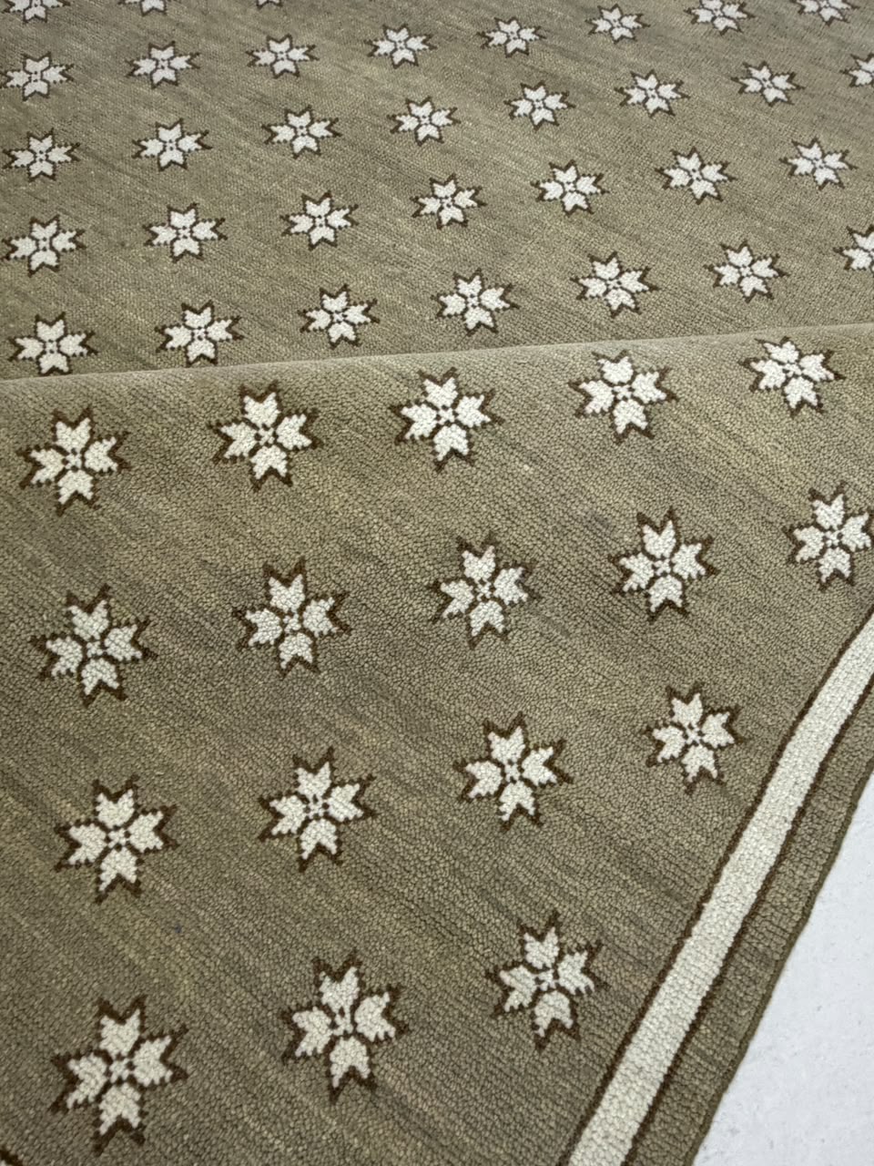 Folded corner of a taupe star-patterned rug showing the border and reverse side.