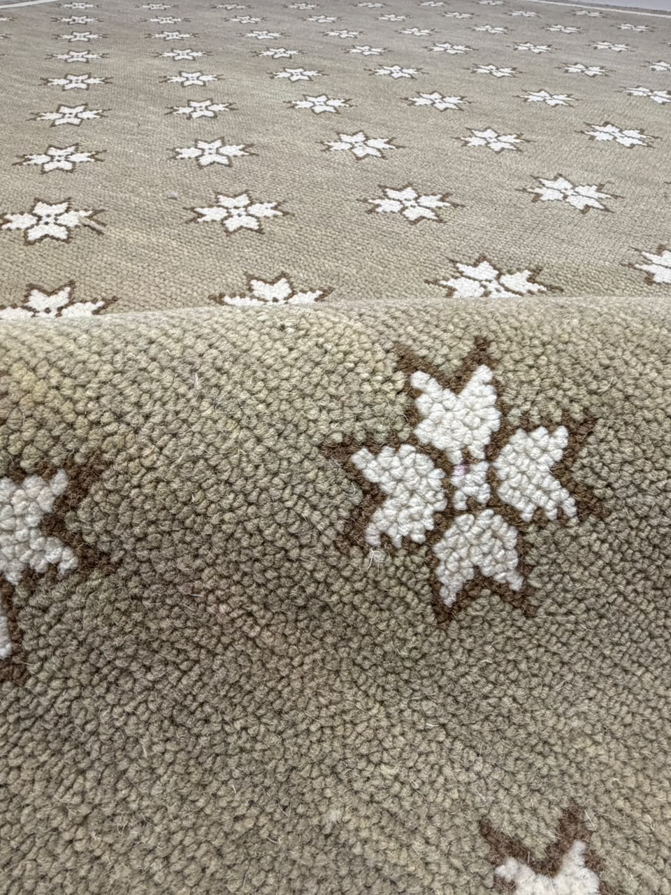 Close-up of taupe rug texture with an ivory star motif outlined in dark brown.