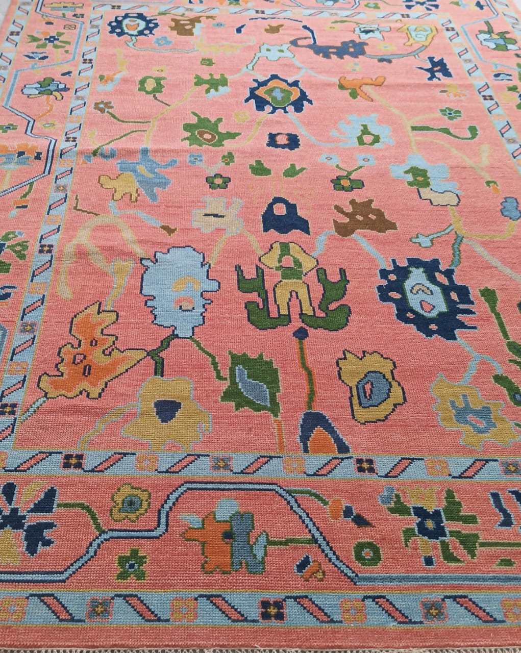 Coral pink handwoven Oushak rug with colorful floral motifs and decorative border