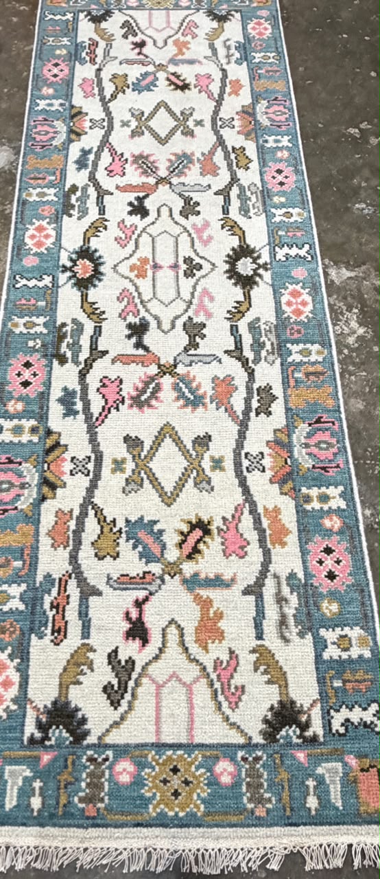 Cream floral runner rug with dusty teal-blue borders, colorful traditional motifs and fringe.