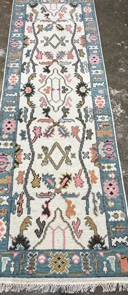 Cream floral runner rug with dusty teal-blue borders, colorful traditional motifs and fringe.