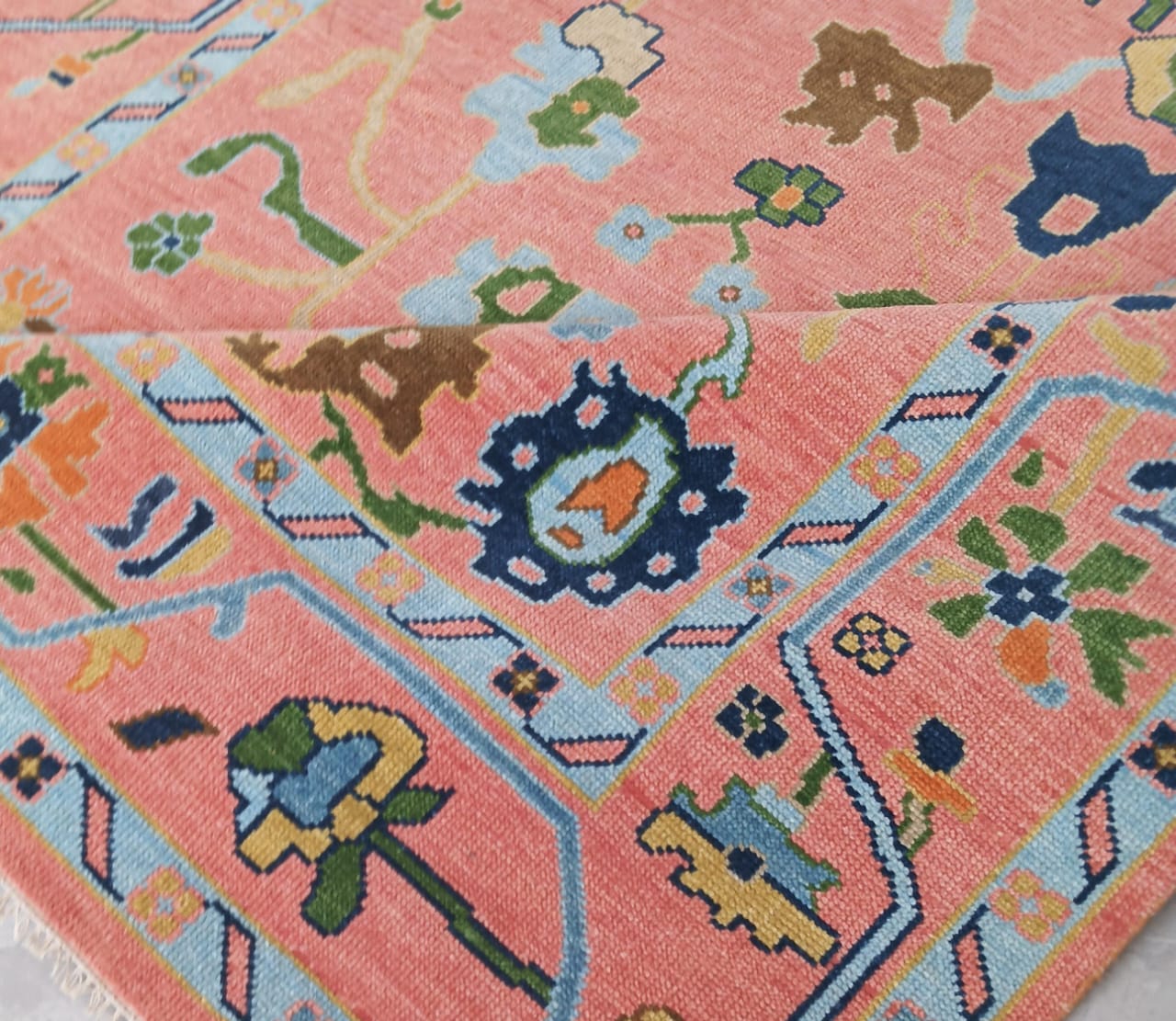 Close-up of a colorful patterned rug with geometric shapes and floral elements on a pink background.