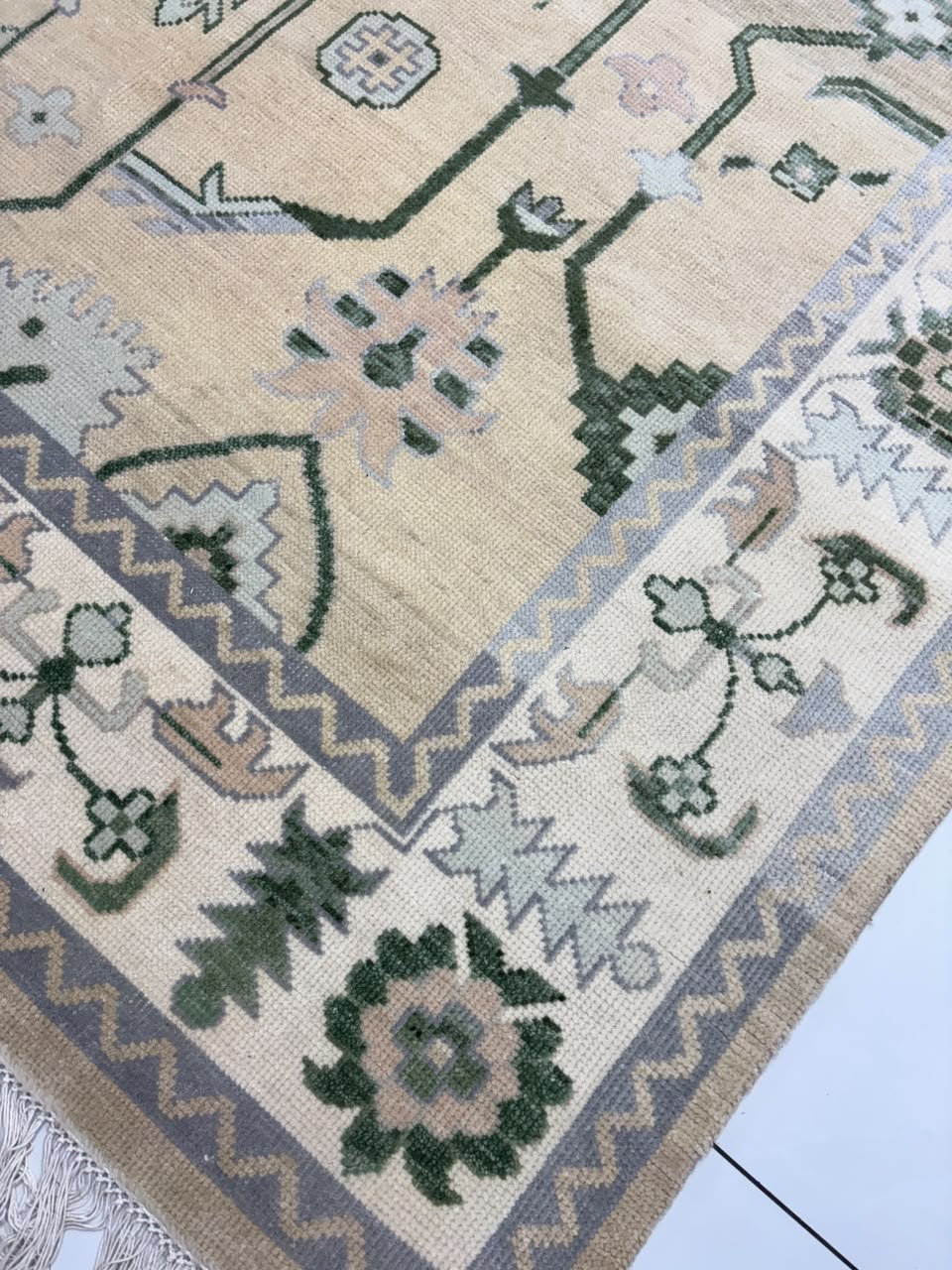 Beige Oushak-inspired rug corner with sage green motifs and fringed edge