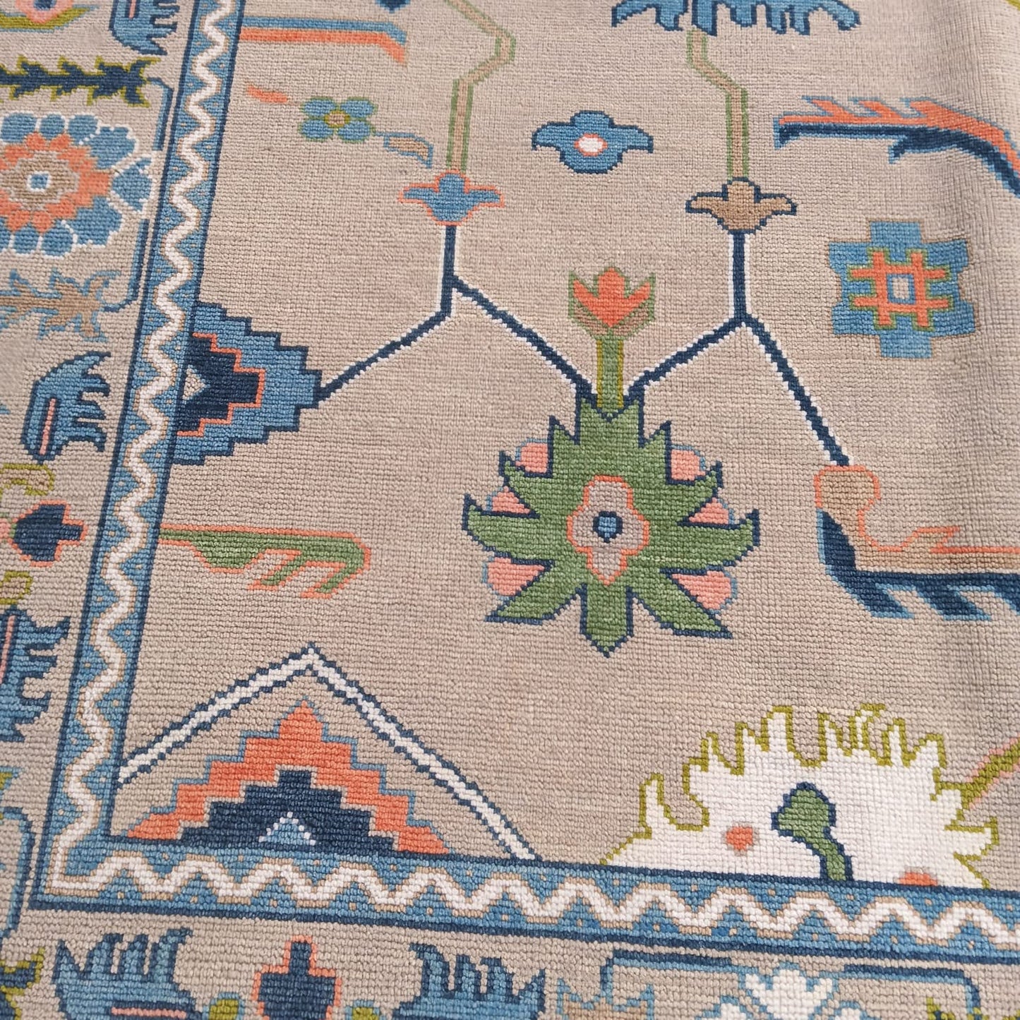 Handwoven wool Oushak rug featuring a beige background with dusty blue, coral and sage green floral pattern.