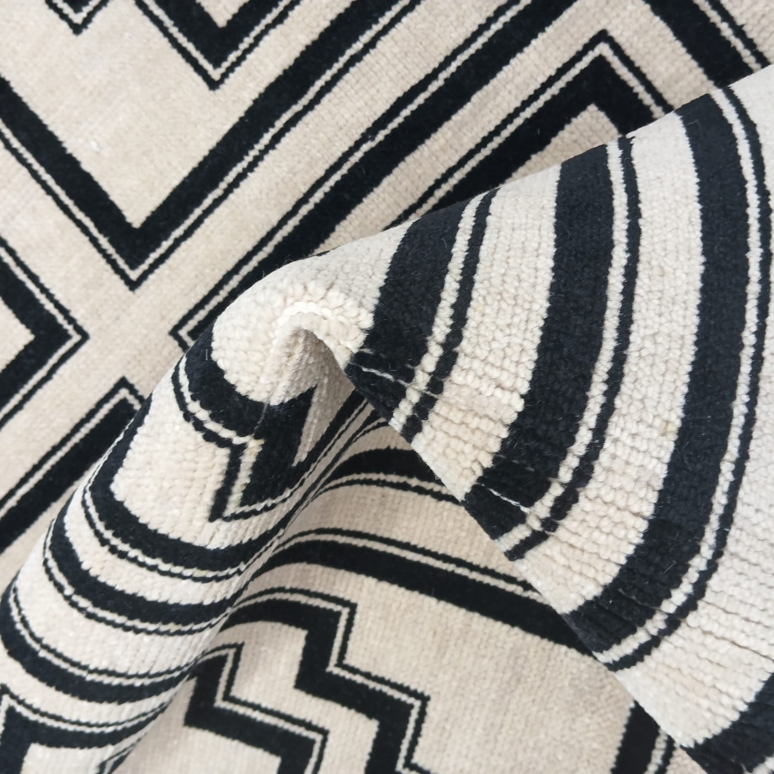 Folded corner view of black and ivory handwoven geometric wool rug
