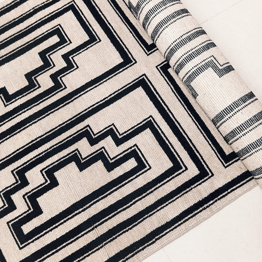 Angled view of black and ivory geometric handwoven wool rug

