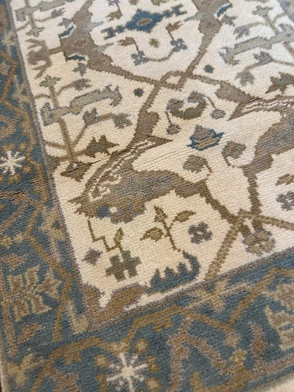 Handmade tribal rug with animal motifs and dusty blue border on ivory background