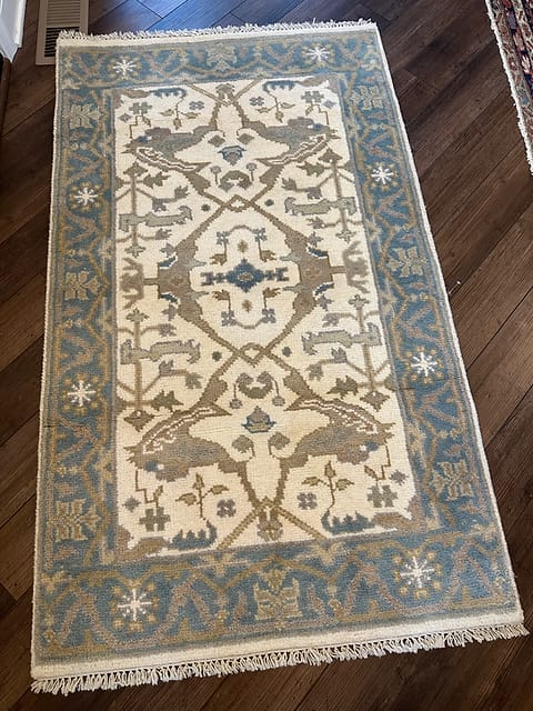 Handmade tribal Oushak rug in blue and ivory displayed on dark wood flooring