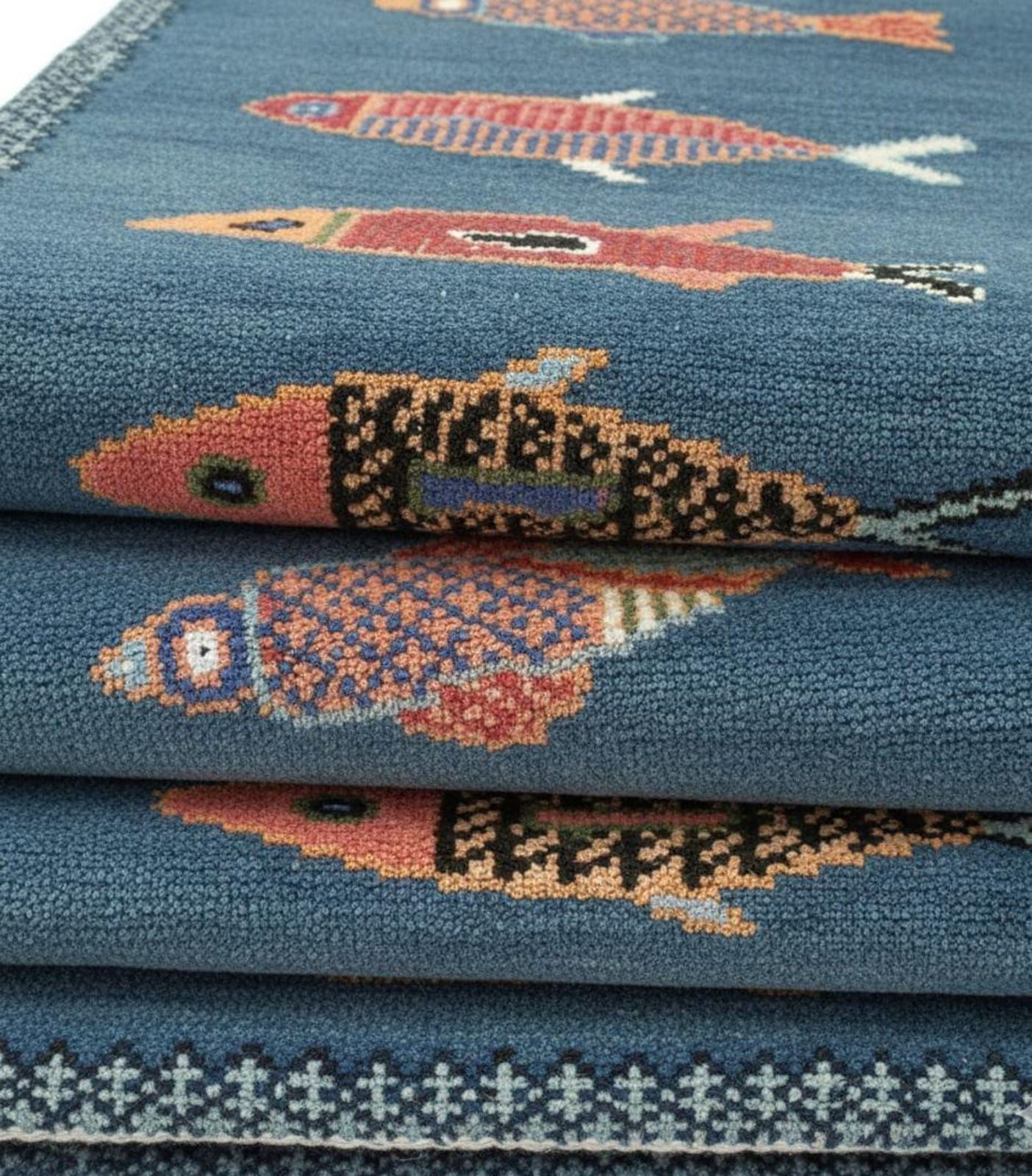 Folded handmade blue fish runner rug showing thickness and weave texture