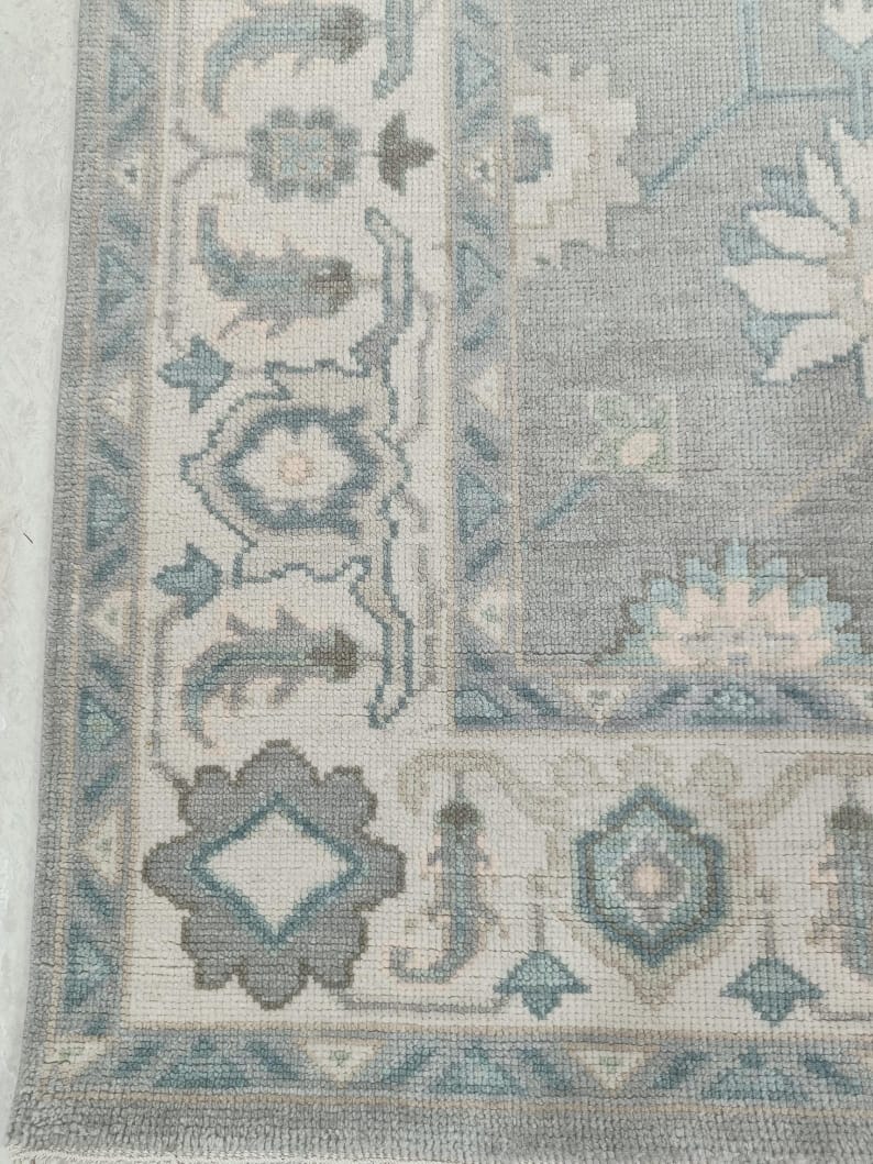 Close up of blue grey Oushak rug border with ivory and teal floral pattern