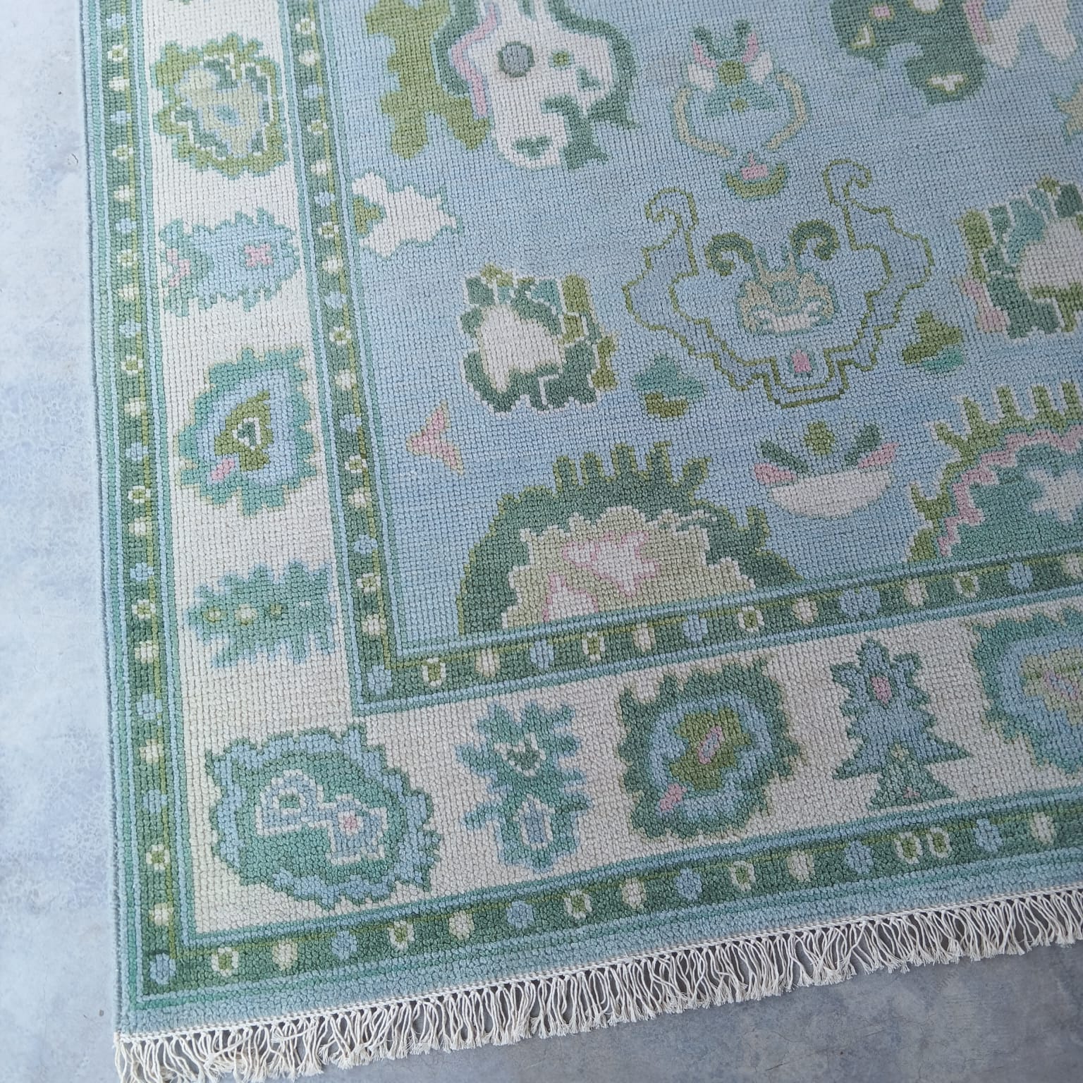 Corner detail of blue and ivory handwoven wool rug with traditional fringe edging