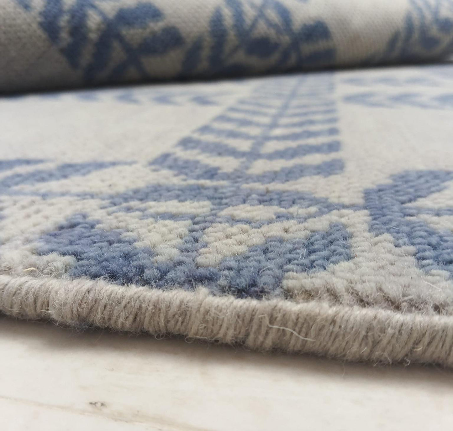 Low pile blue and ivory handwoven wool rug edge detail showing flatweave thickness and geometric pattern texture