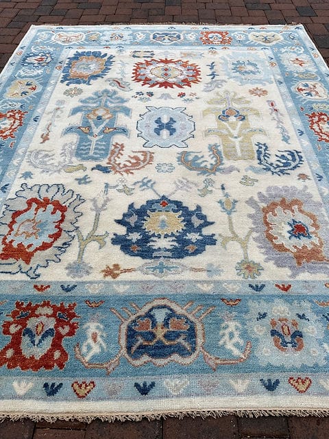 Large handmade Oushak area rug in ivory and sky blue featuring traditional floral medallion design