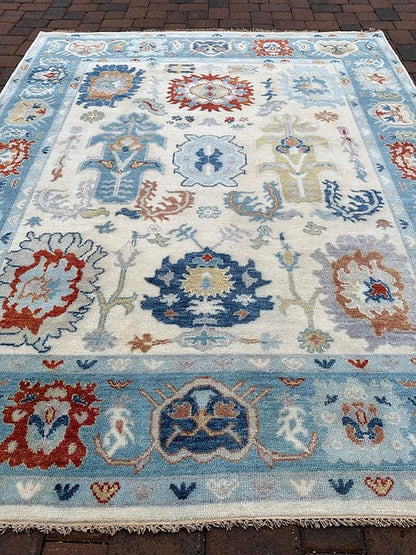 Large handmade Oushak area rug in ivory and sky blue featuring traditional floral medallion design