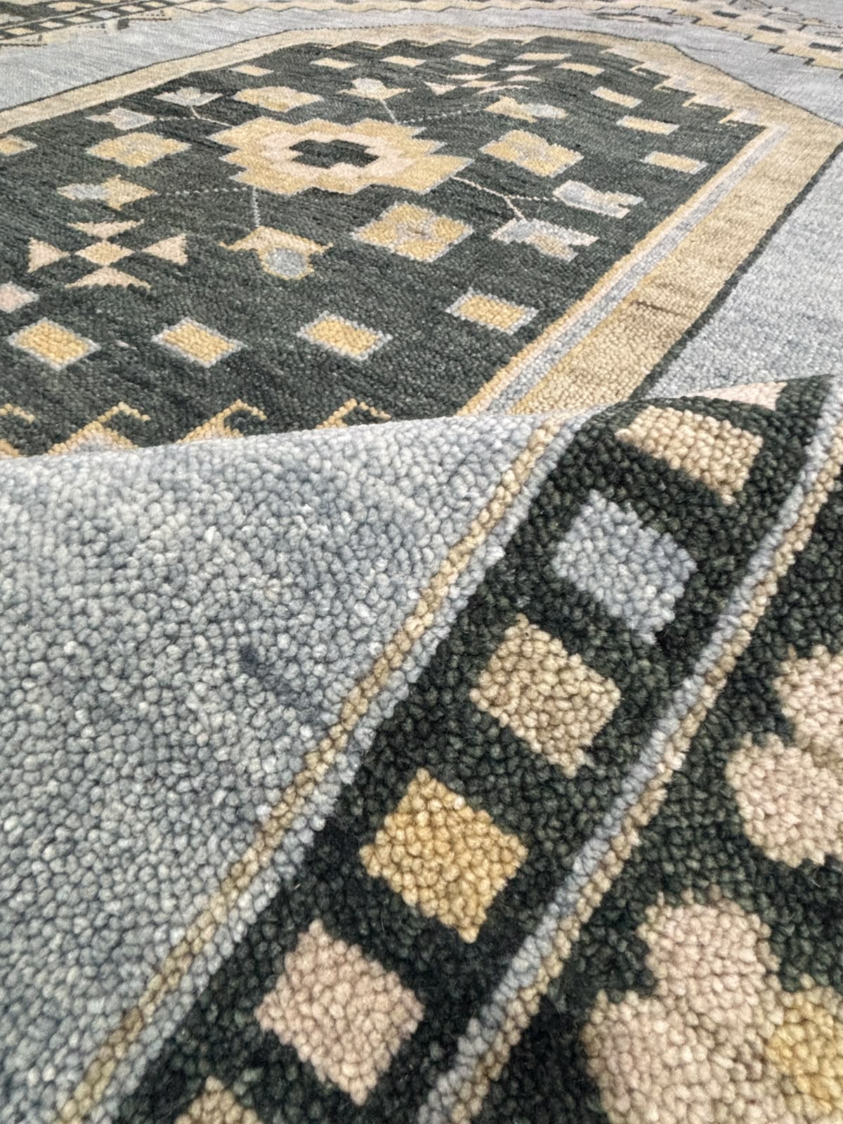 Folded corner of handmade blue Oushak wool rug showing medium pile, dense weave, and premium handcrafted construction