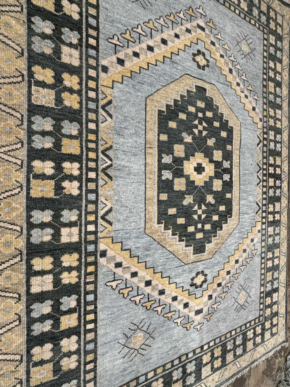 Angled view of handmade blue tribal Oushak rug highlighting geometric medallion and traditional border details.