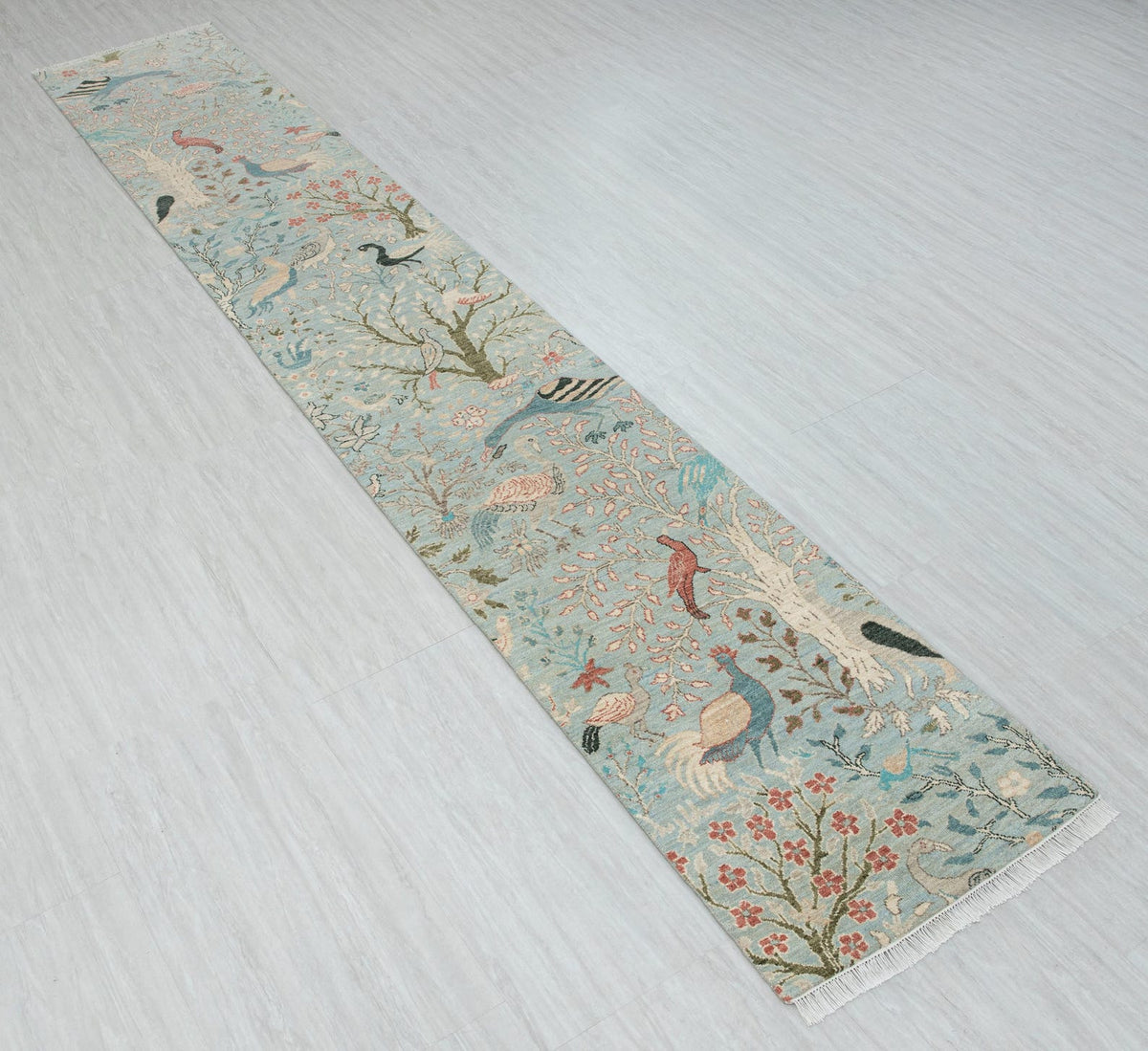Angled view of blue vintage bird runner rug with floral botanical design and fringed ends