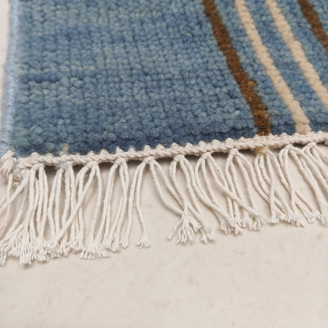 Hand-knotted fringe detail on blue plaid wool area rug