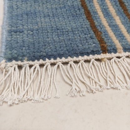 Hand-knotted fringe detail on blue plaid wool area rug