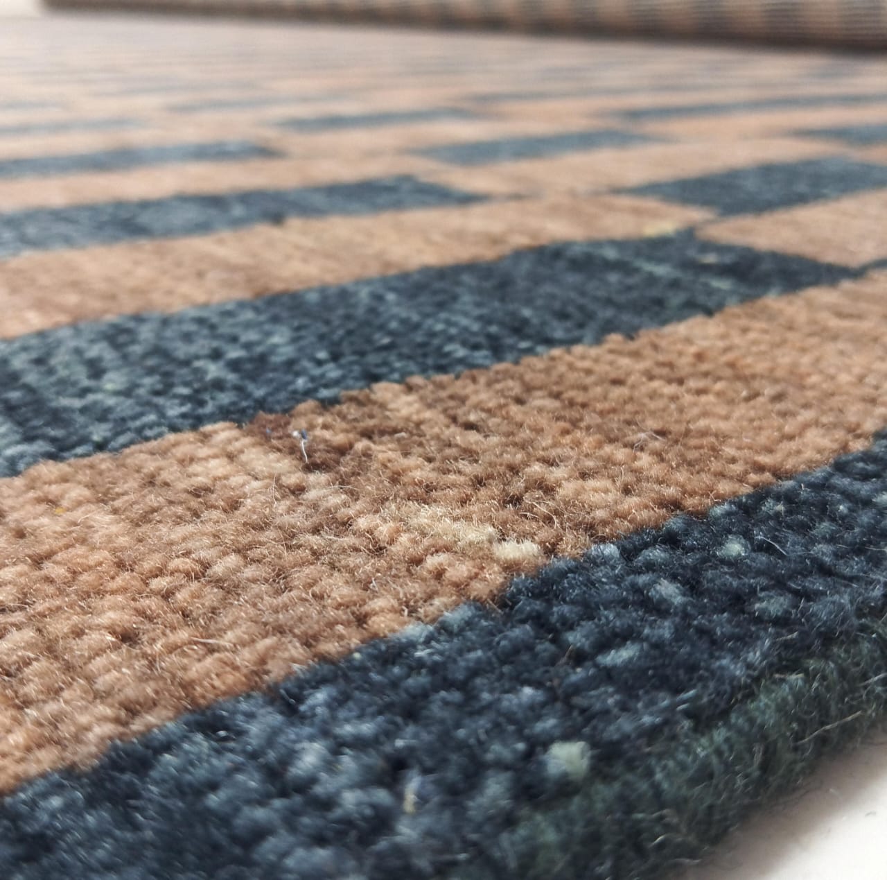 Close-up of wool pile texture on brown and black striped rug
