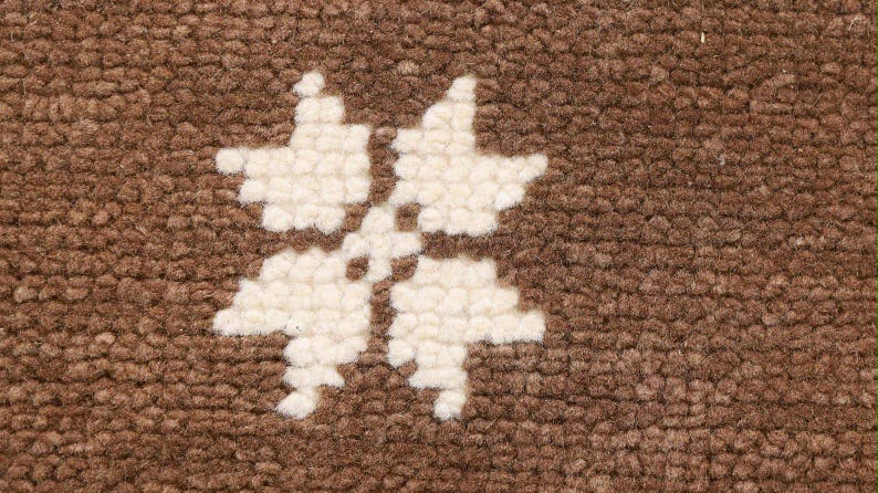 Close-up of an ivory flower motif woven into a brown rug.
