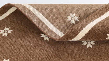 Folded brown floral rug showing its textured surface and ivory motifs.