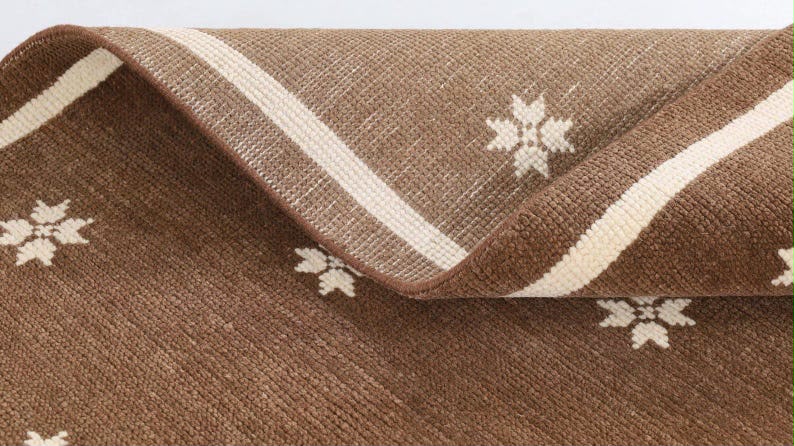 Ivory fringe and border detail on a brown rug with floral motifs.