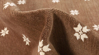 Detailed view of an ivory flower motif on the brown rug surface.