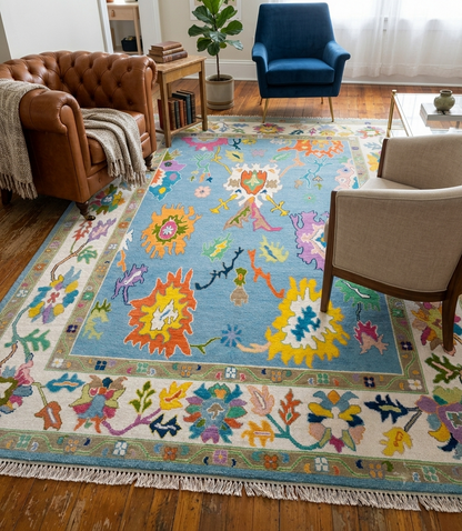 Colorful handmade Oushak area rug featuring a sky blue background and ivory floral border in a contemporary living room.