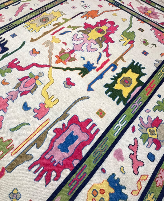 Angled view of a handmade colorful Scandinavian wool area rug with vibrant geometric folk art design and ivory background.