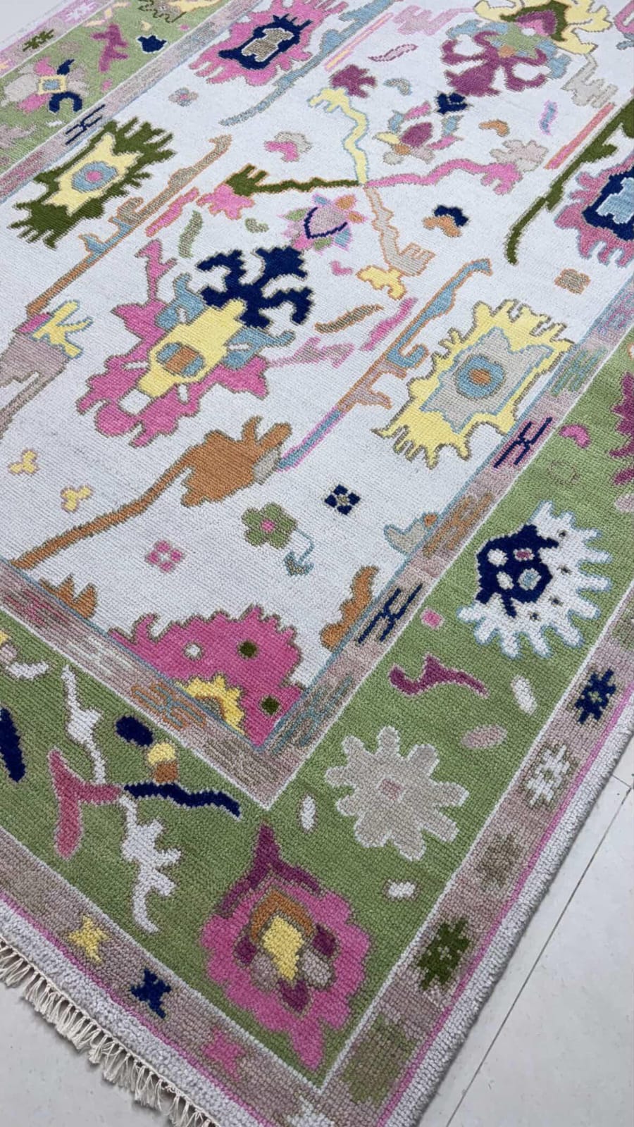 Handmade pastel Oushak rug with colorful floral motifs and sage green border on ivory background