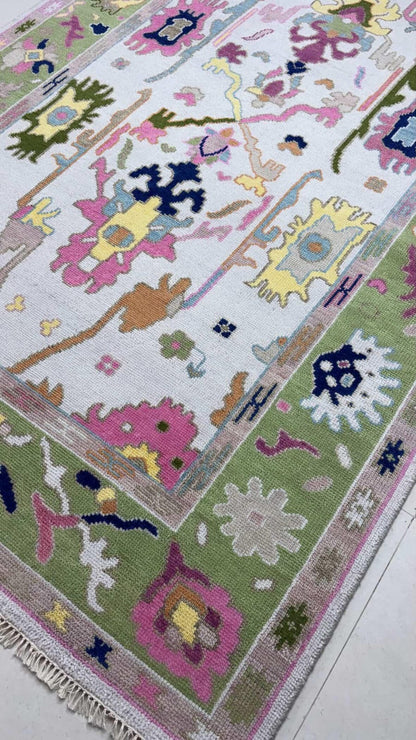 Handmade pastel Oushak rug with colorful floral motifs and sage green border on ivory background