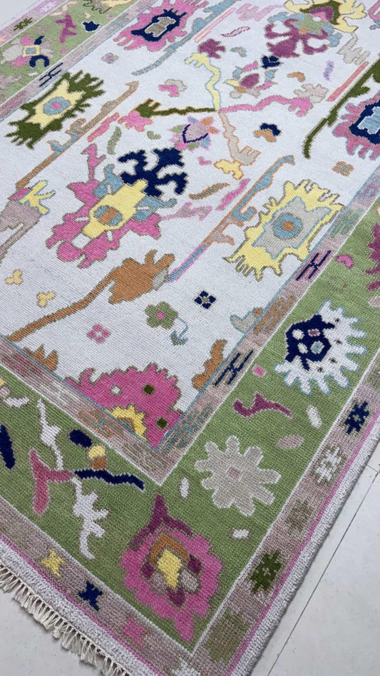 Handmade pastel Oushak rug with colorful floral motifs and sage green border on ivory background