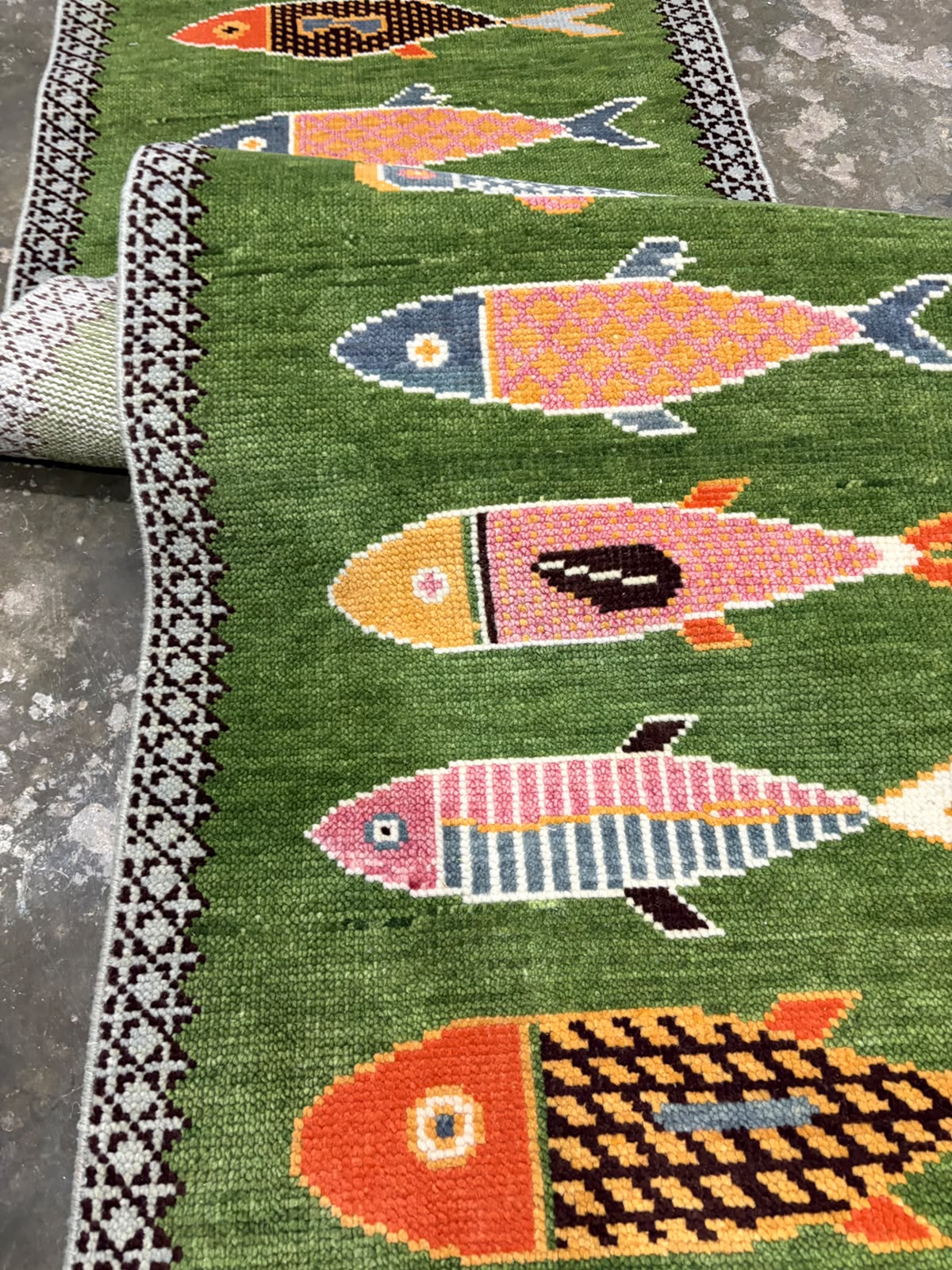 Close-up of the medium pile wool texture and colourful details of a hand-knotted green rug