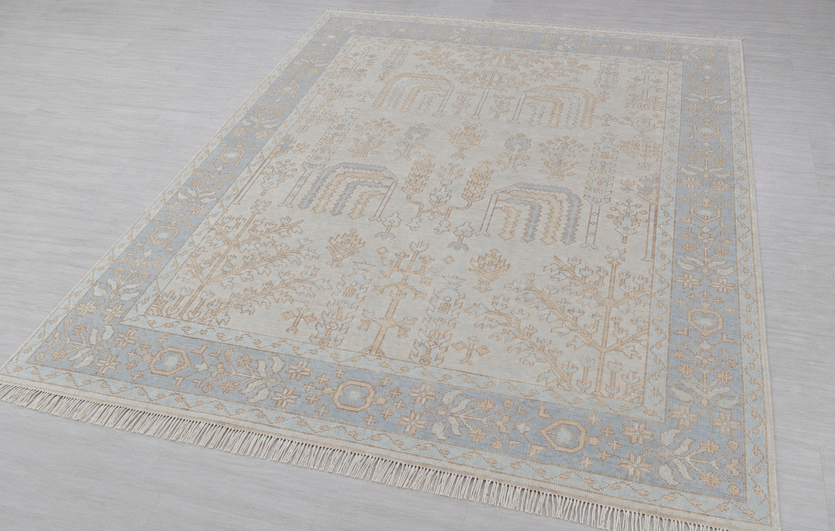 Cream and blue vintage floral rug with ornate border shown from an angled view