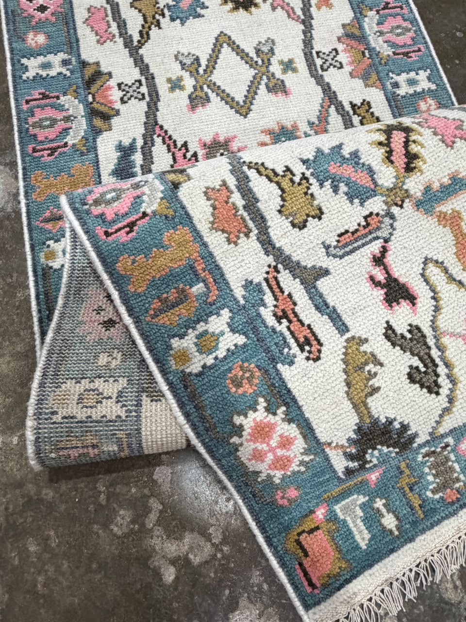 Cream floral runner rug with dusty teal-blue borders, colorful traditional motifs and fringe.