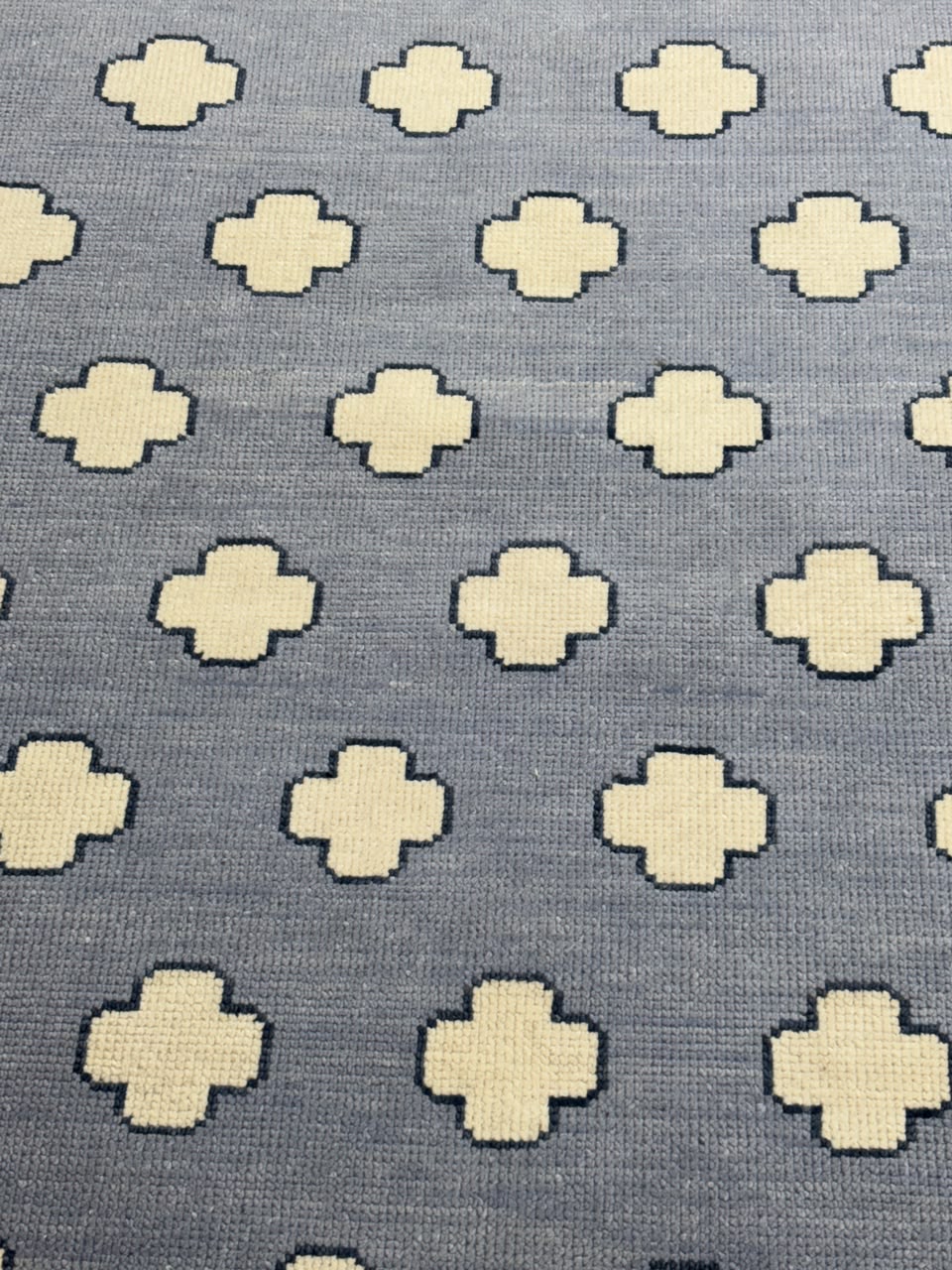 A close-up of a woven textile pattern featuring cream-colored geometric cross motifs on a slate blue-gray background.